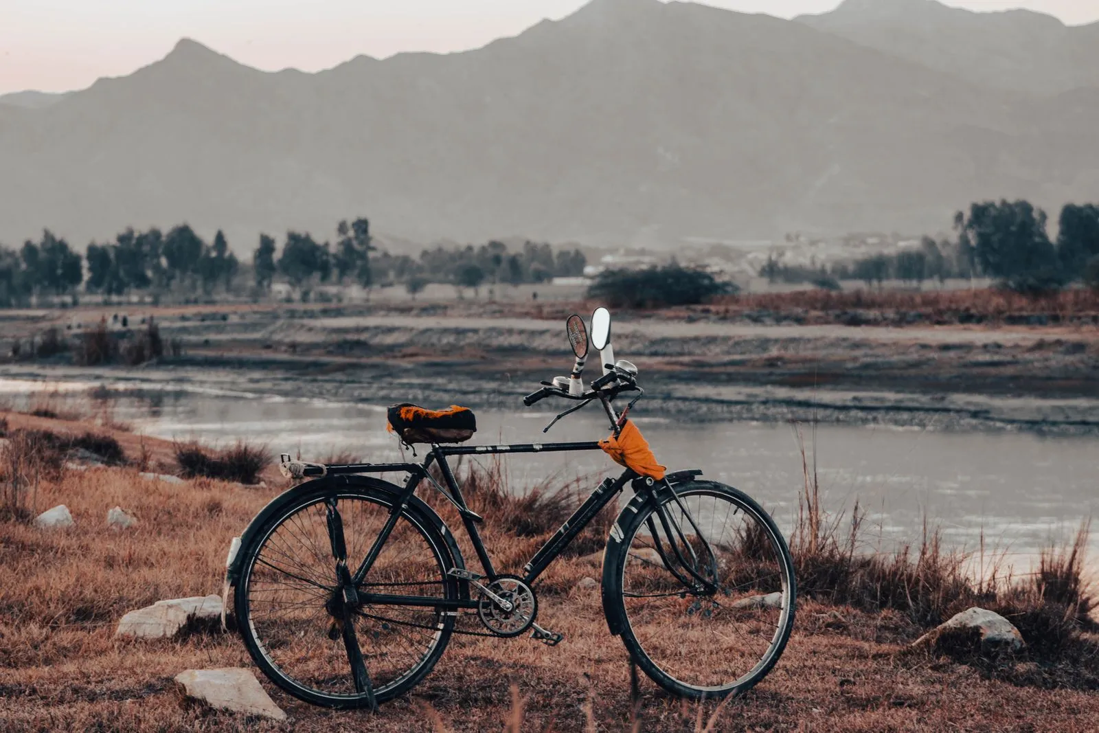 A tranquil view of a vintage bicycle by a serene mountain range and river at twilight.